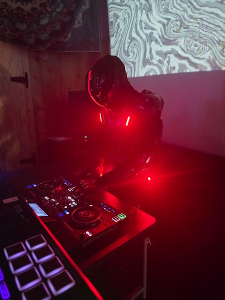 DJ bathed in red light working the decks while a projection glows on the wall