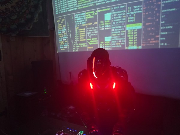 Masked performer behind the decks with code projected overhead during the July 31 event
